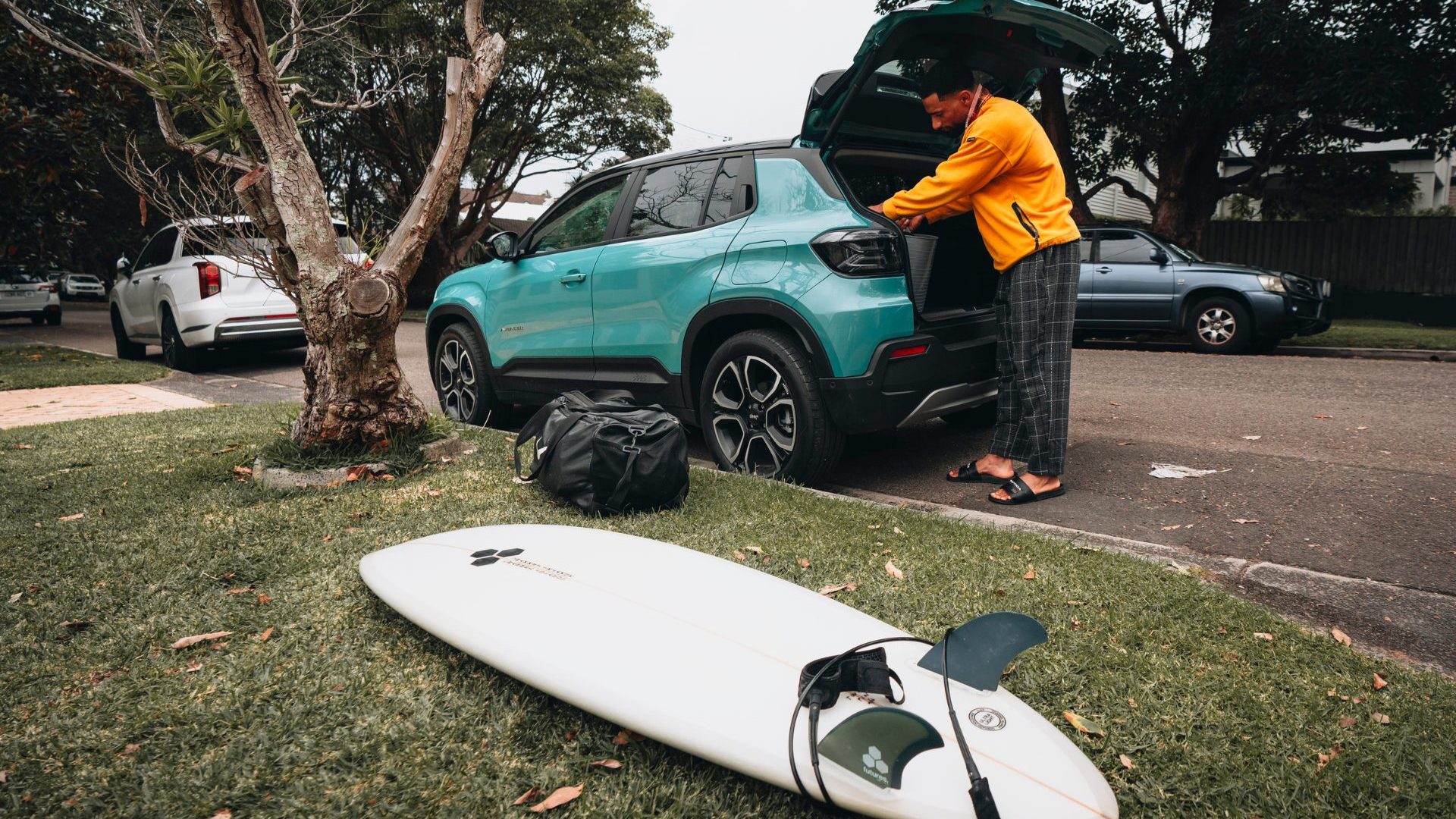 Man packs luggage, including surf board, into boot of blue electric vehicle