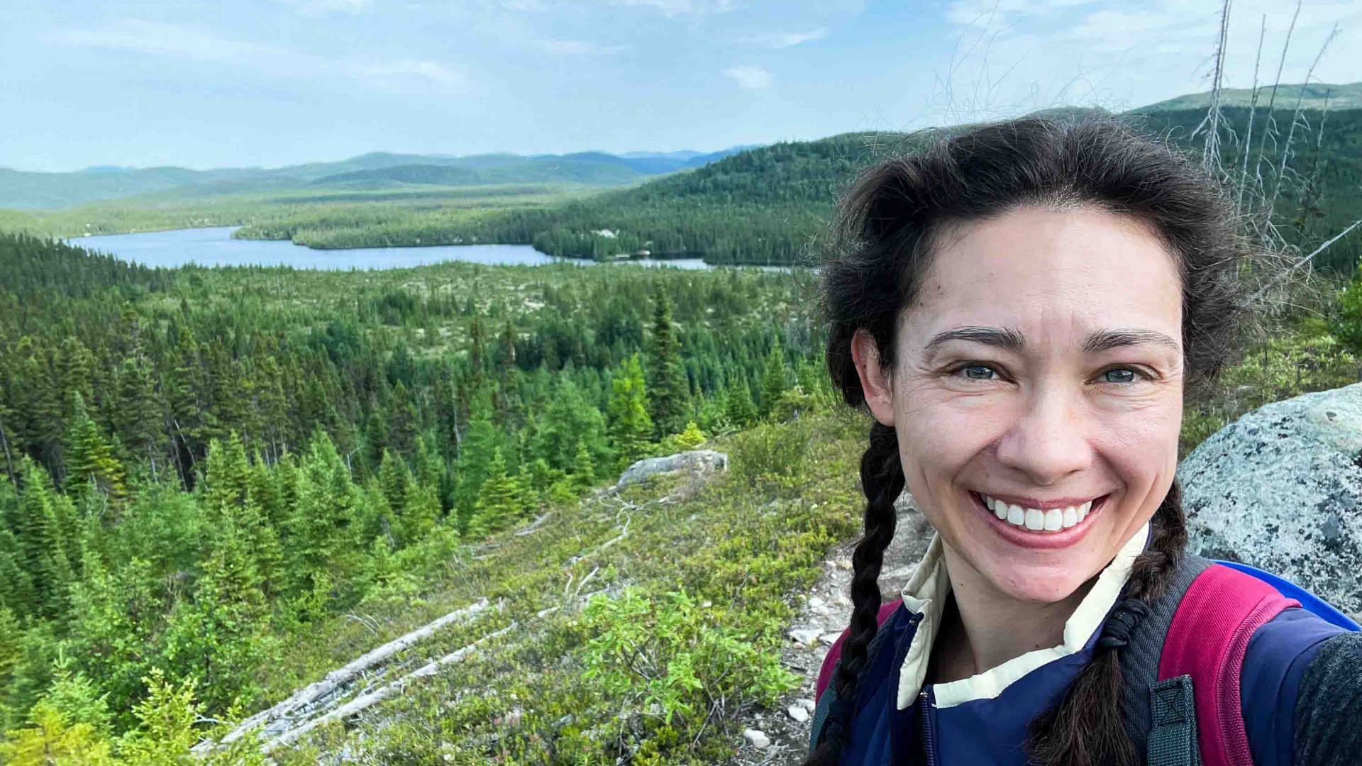 A woman smiles in front of a vista of green hills and lakes.