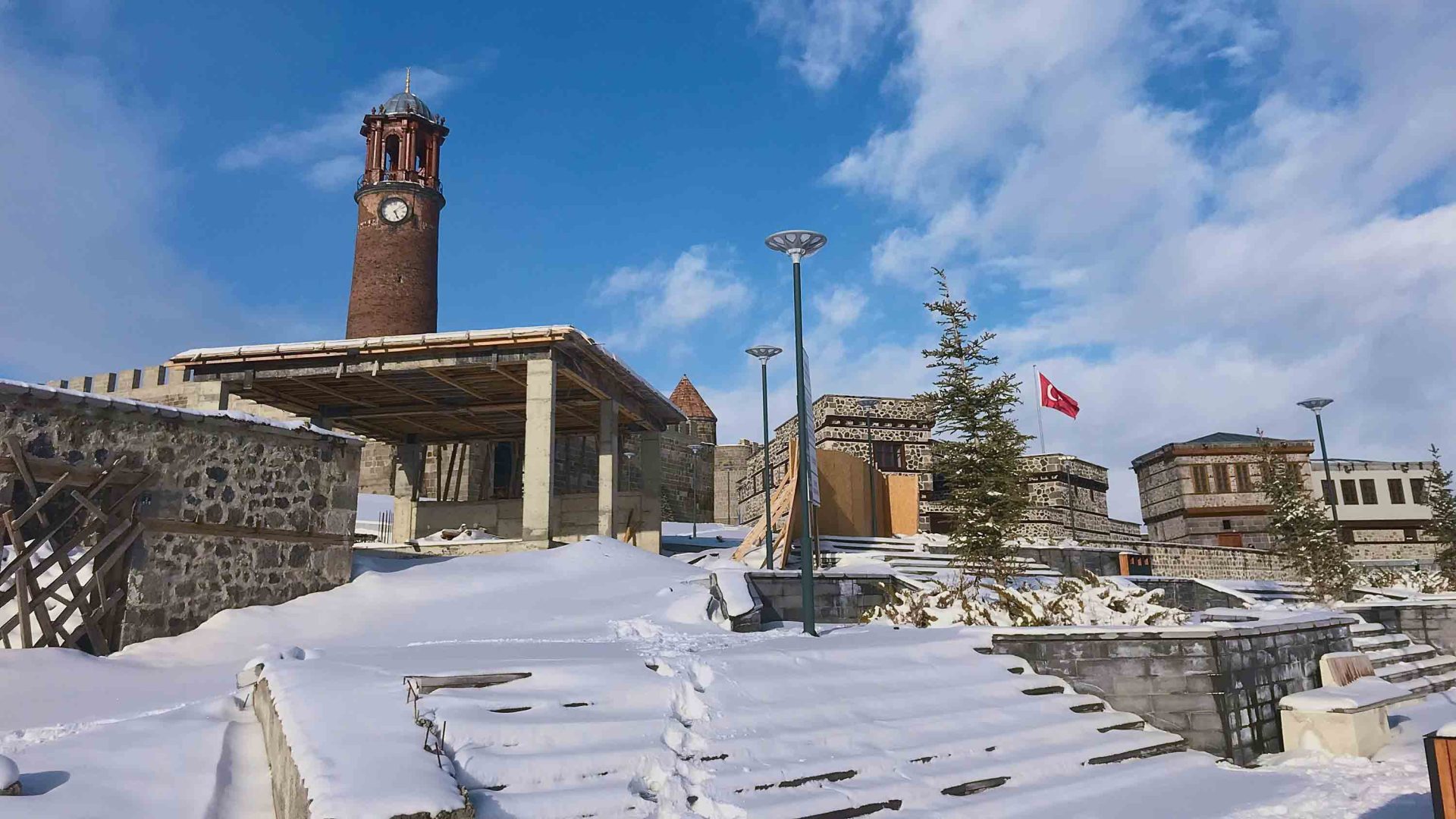 Snow-covered steps lead up to a series of ancient buildings, a Turkish flag flying above one.