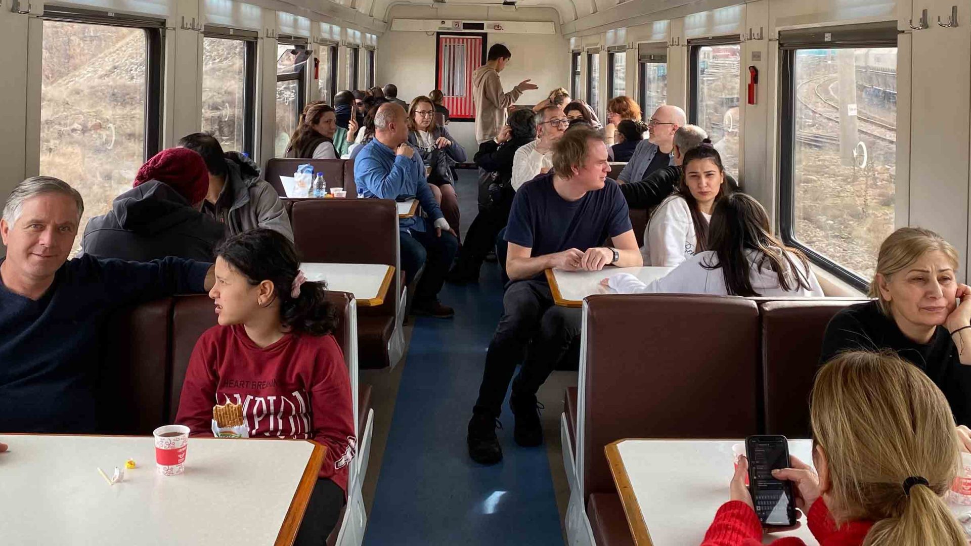 Passengers eat and chat at tables in the dining car.
