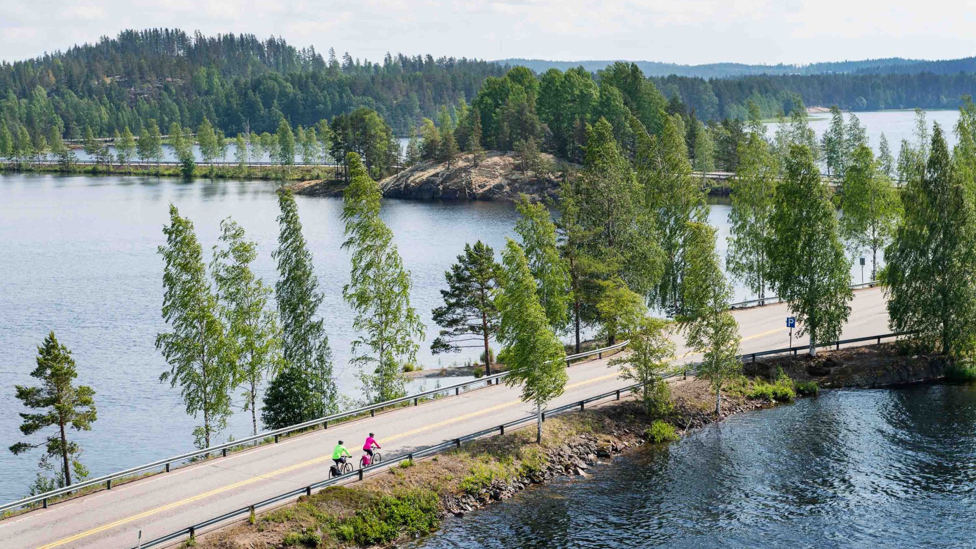 People cycle on a path past a lake.