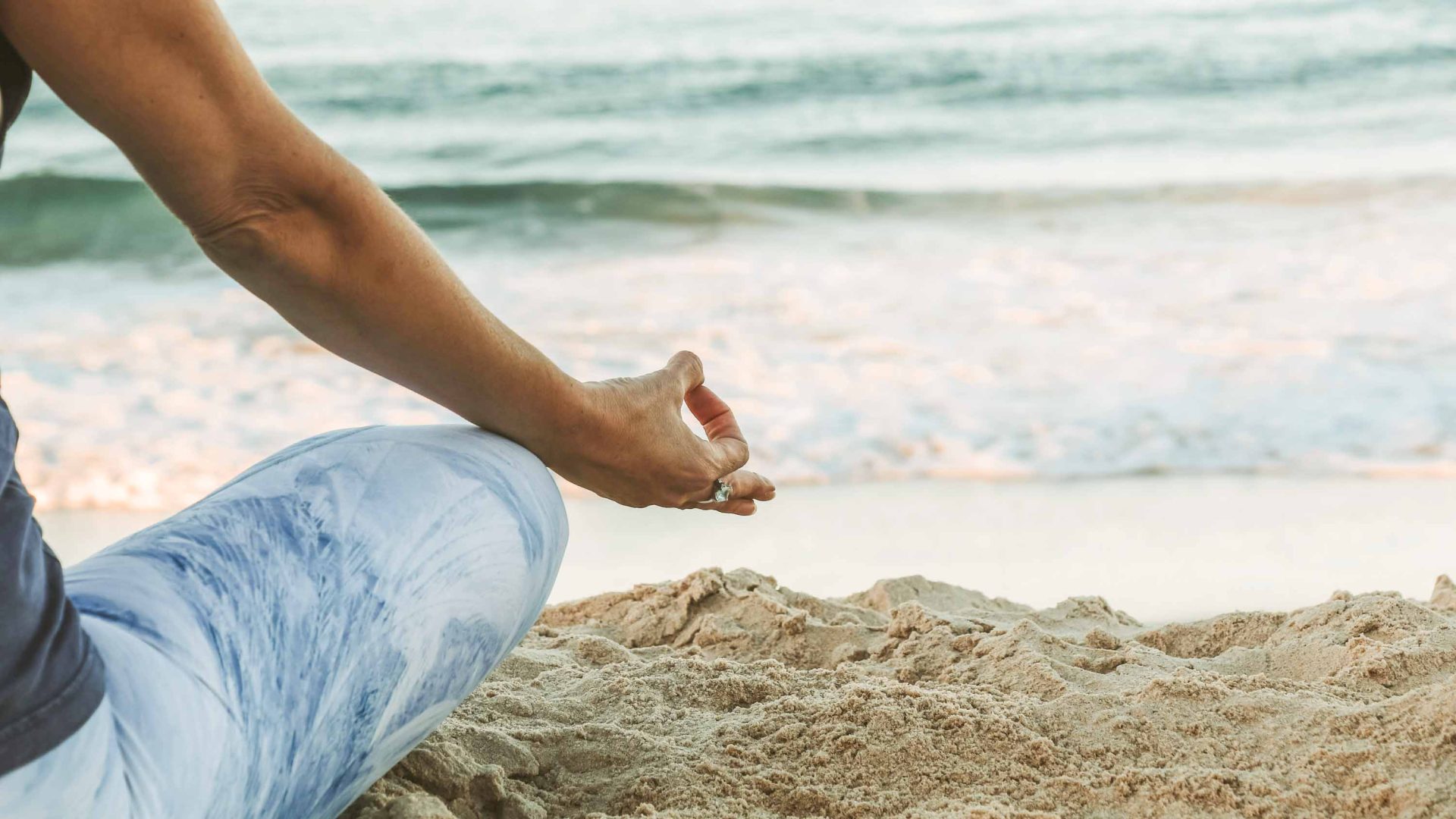 A woman meditates on the sand by the sea.