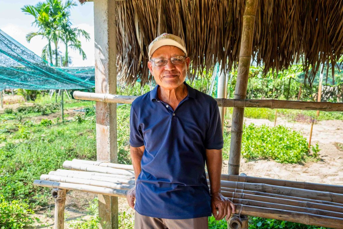 A man stands under a shelter in a garden.