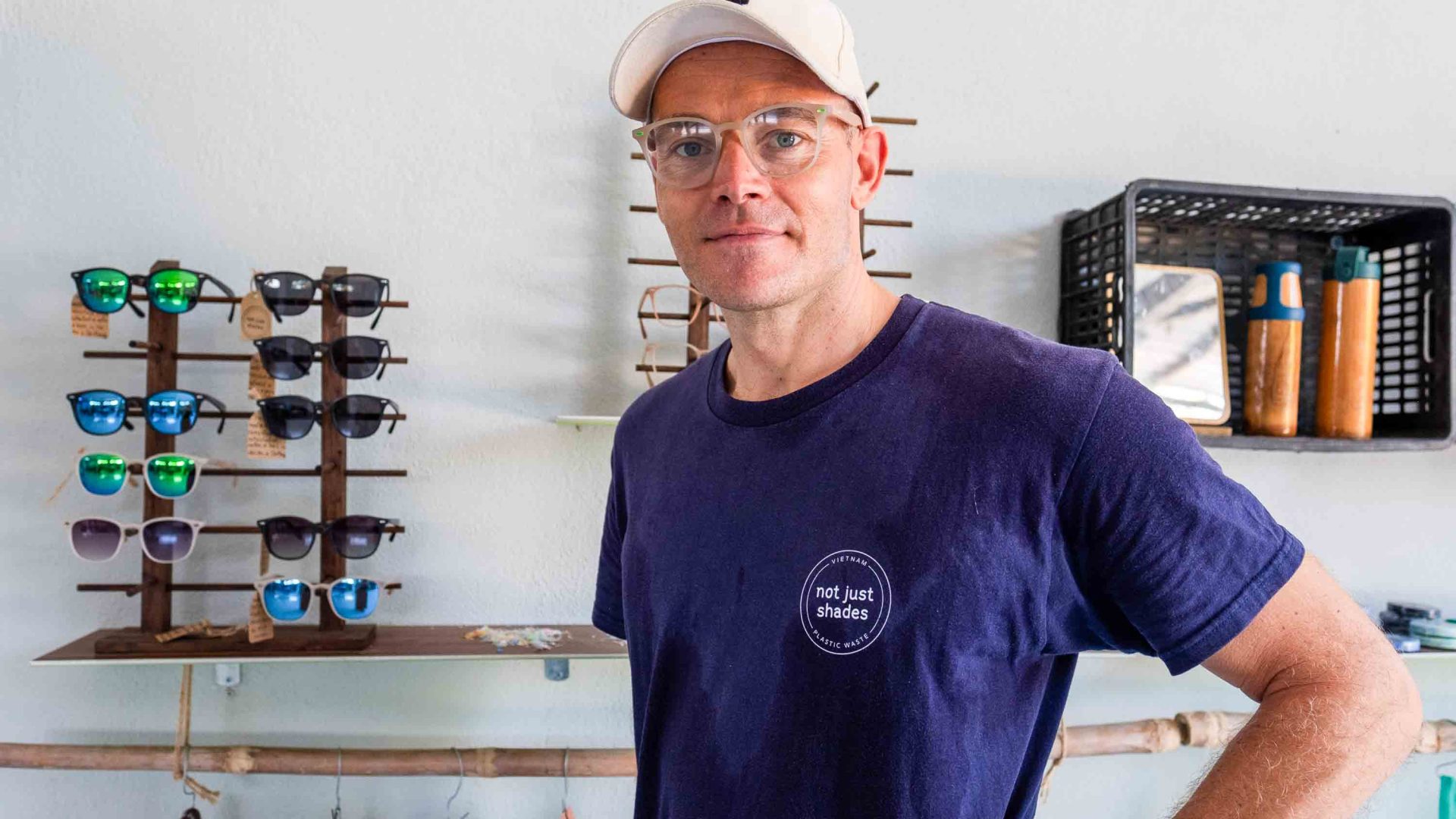 A man stands in front of a display of sunglasses.