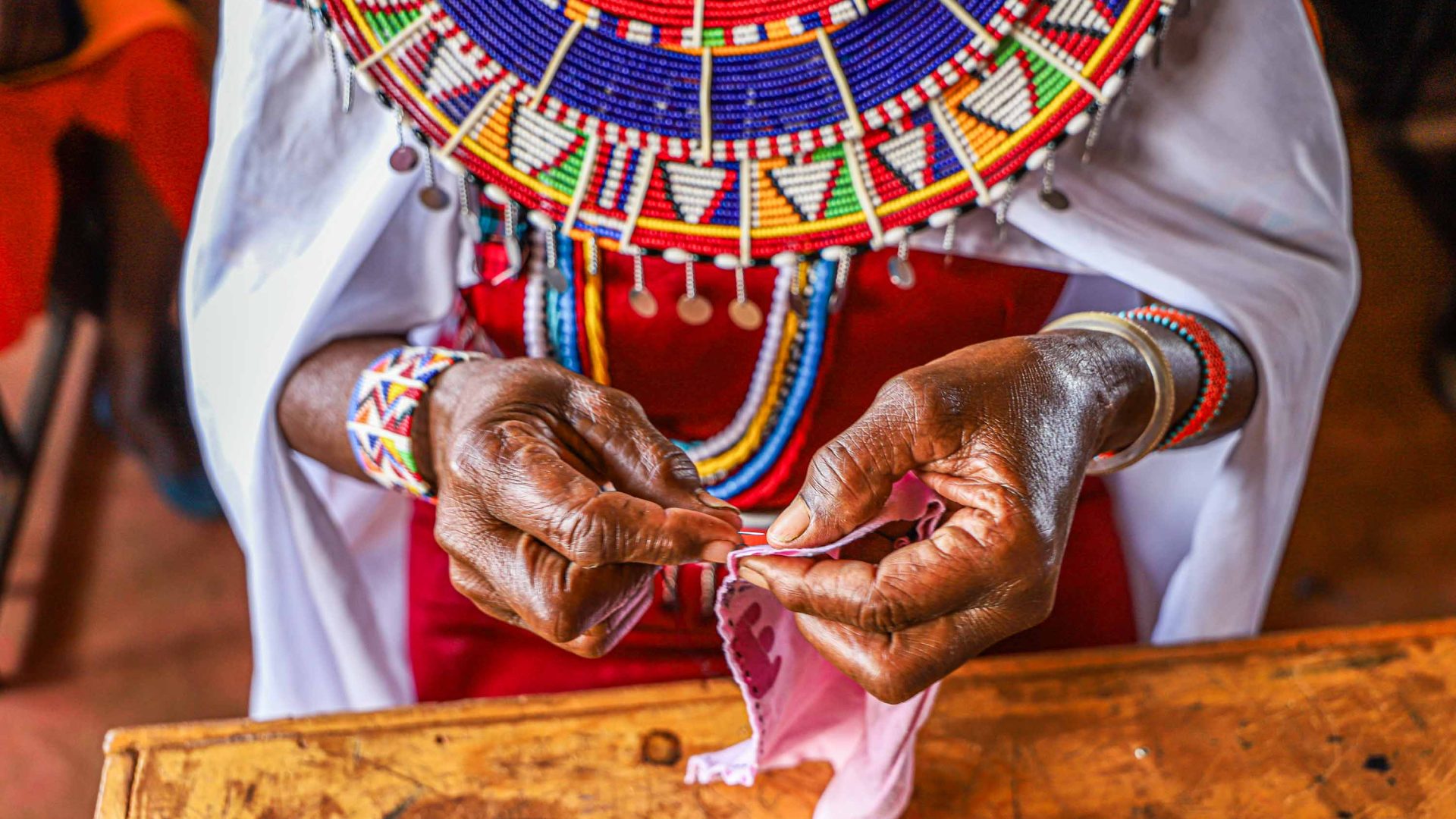 A close up of a Massai womans hands sewing a piece of fabric.
