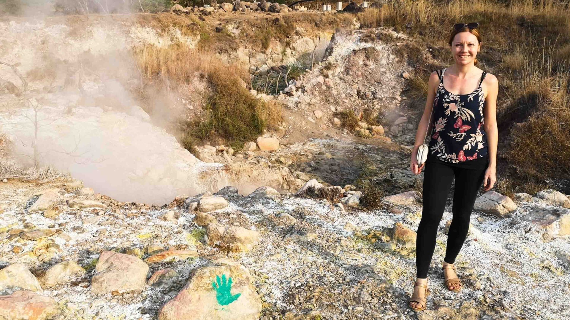 A woman stands by some hot springs.