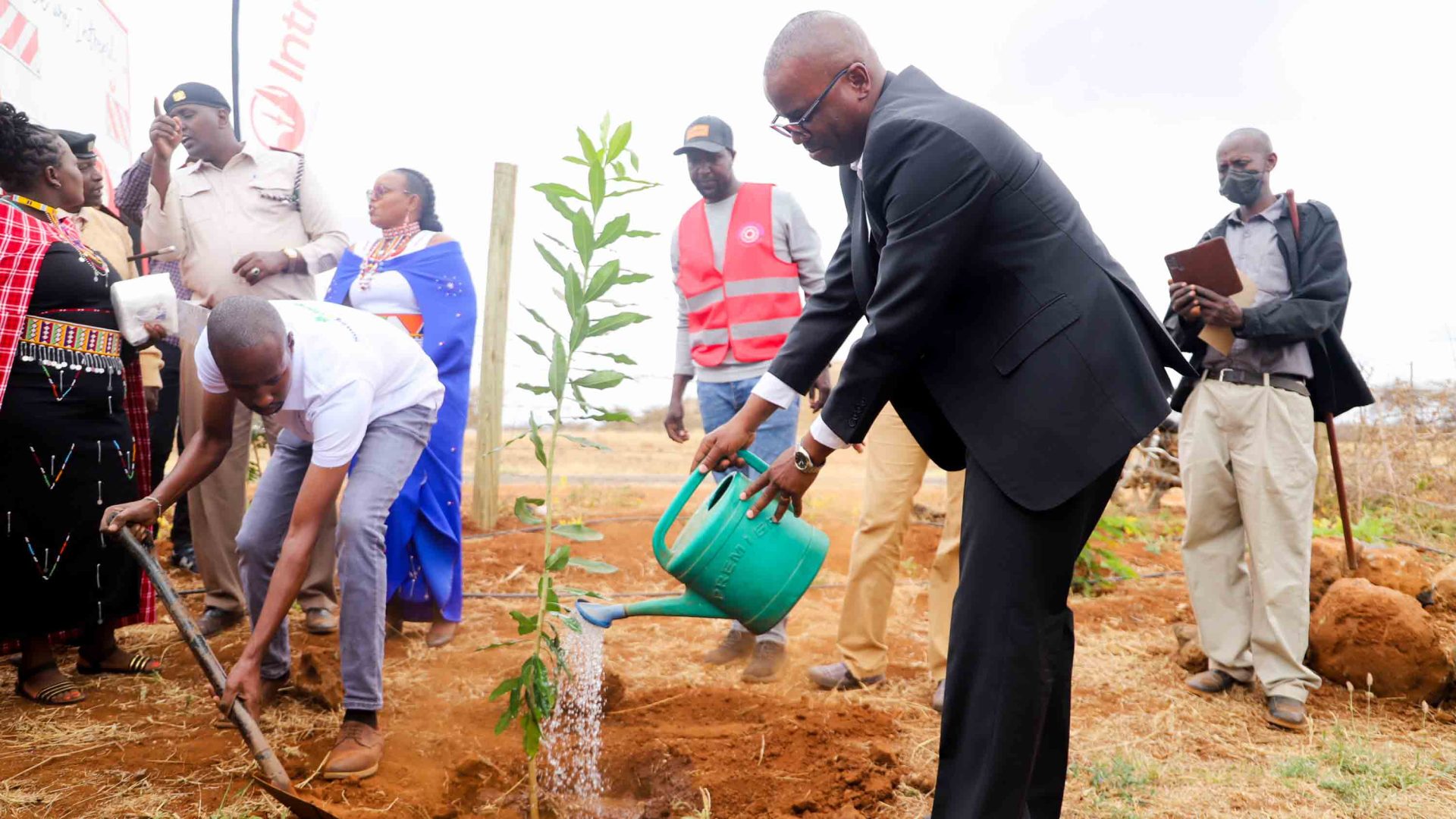 A man plants a tree while others are in the background.