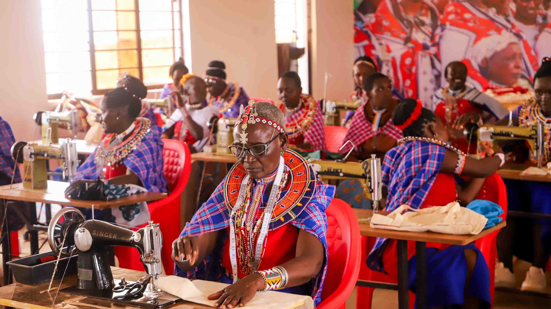 Many women sit at sewing machines and sew.