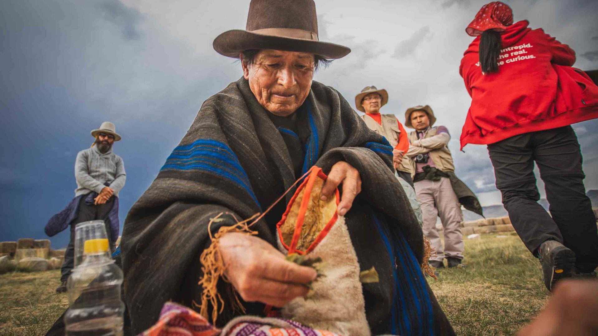 A man in traditional clothing and hat bends over some fabric.