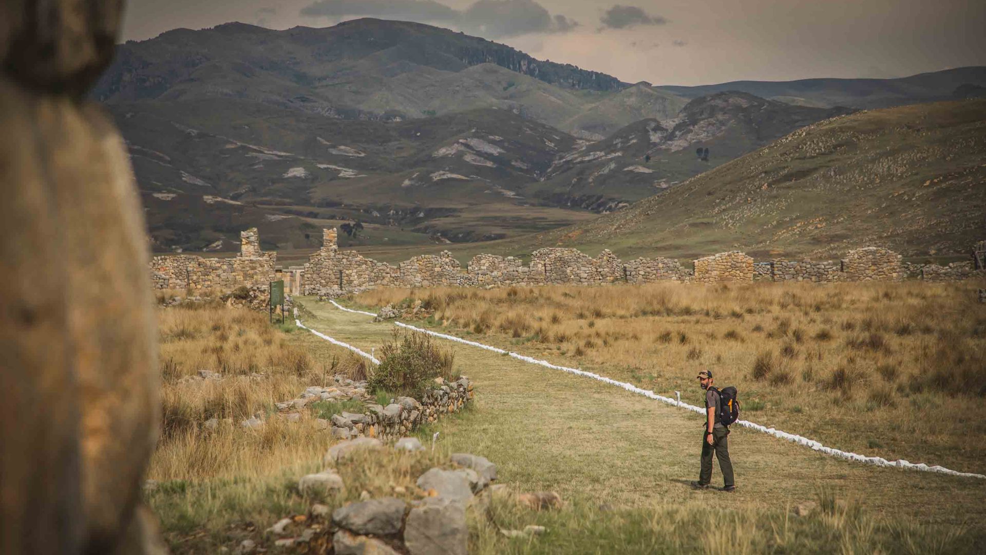 A person looks to the side as he walks towards some ruins.