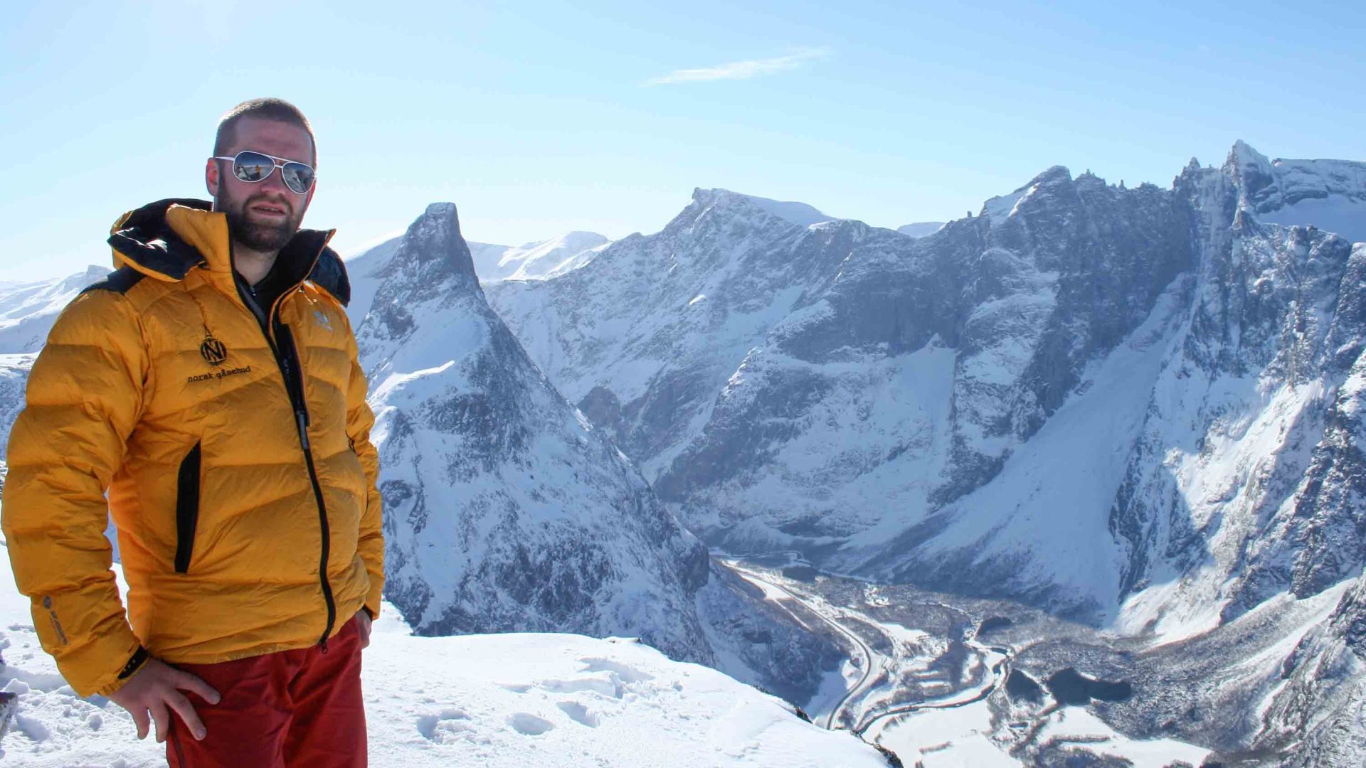 A man stands against snowy mountains.
