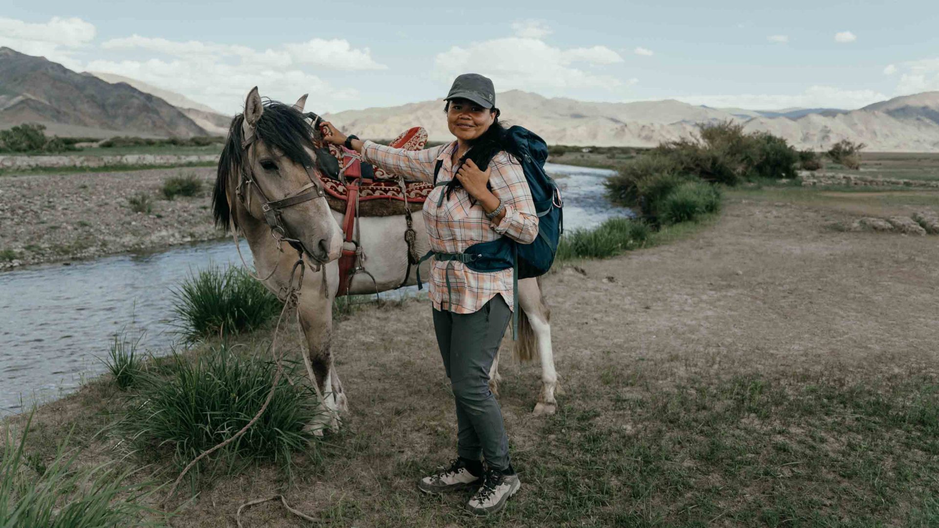 A woman stands with a horse by a lake.