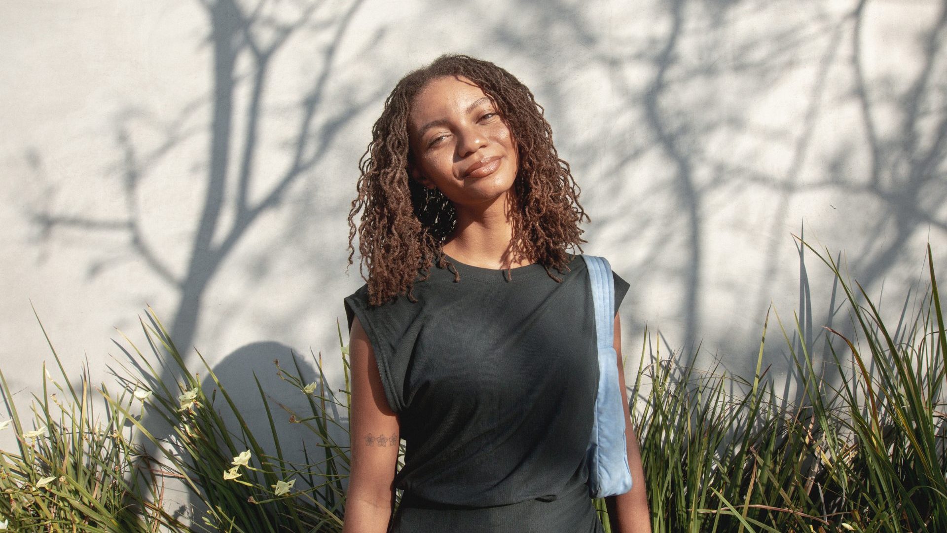 Woman stands in front of green reads against a shadowed wall and smiles