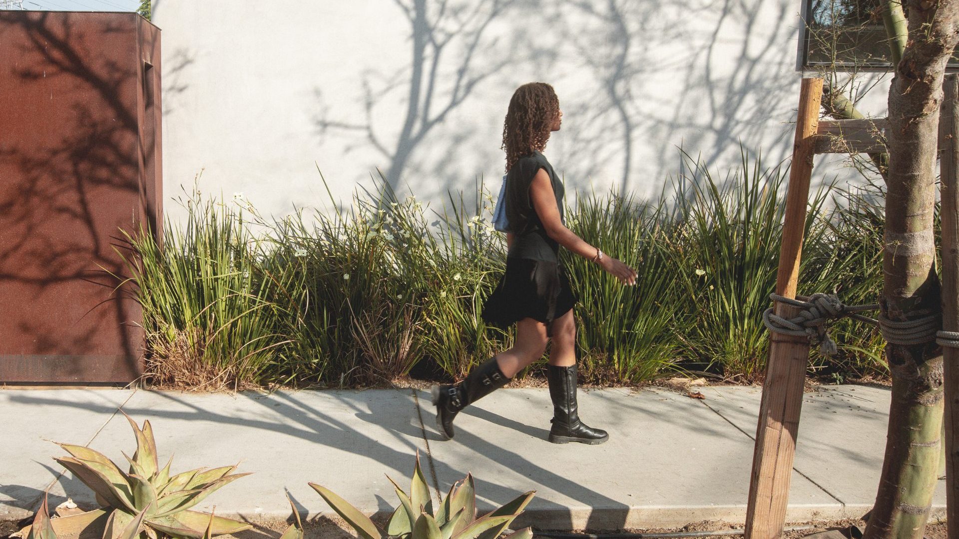 Woman walks down street lined with green plants