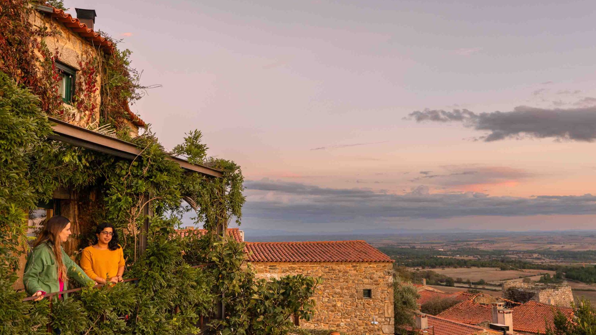 Two women stand on the porch of a guesthouse overlooking a valley.
