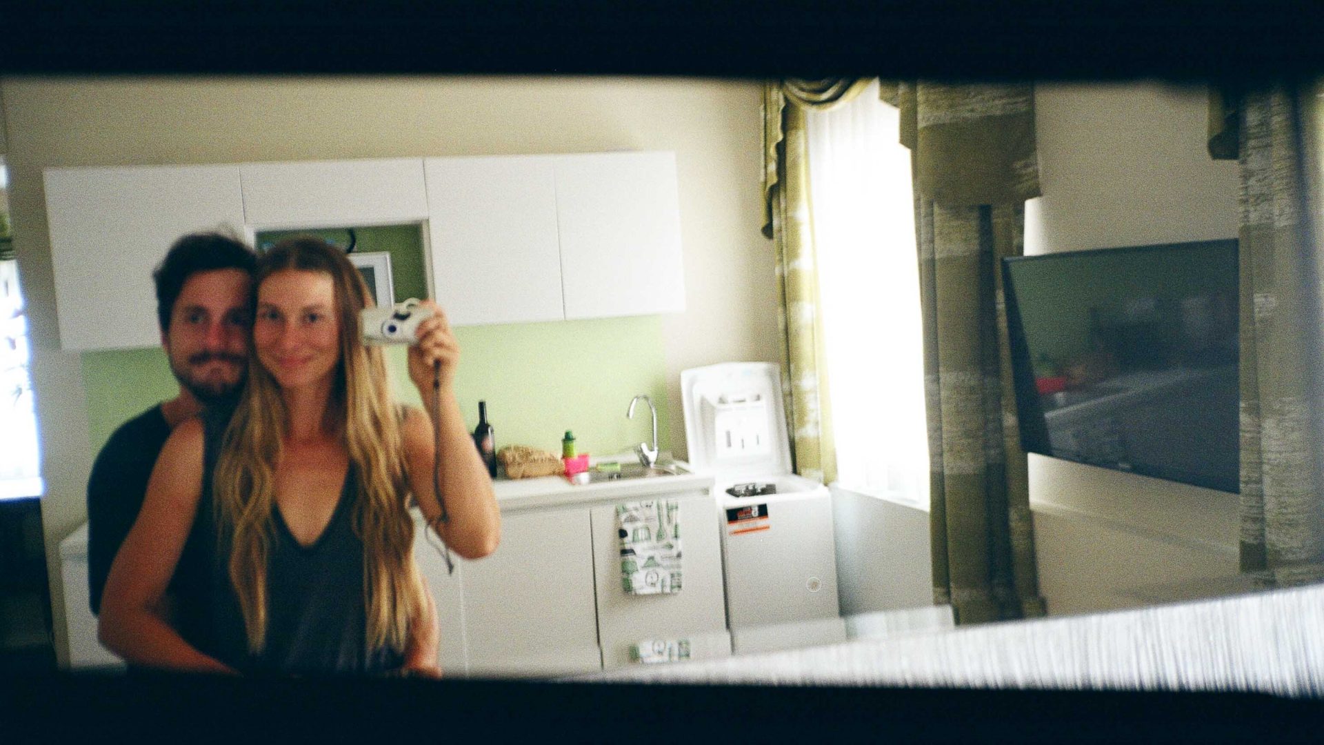 A man and a woman take a photo of their reflection in a mirror at home.