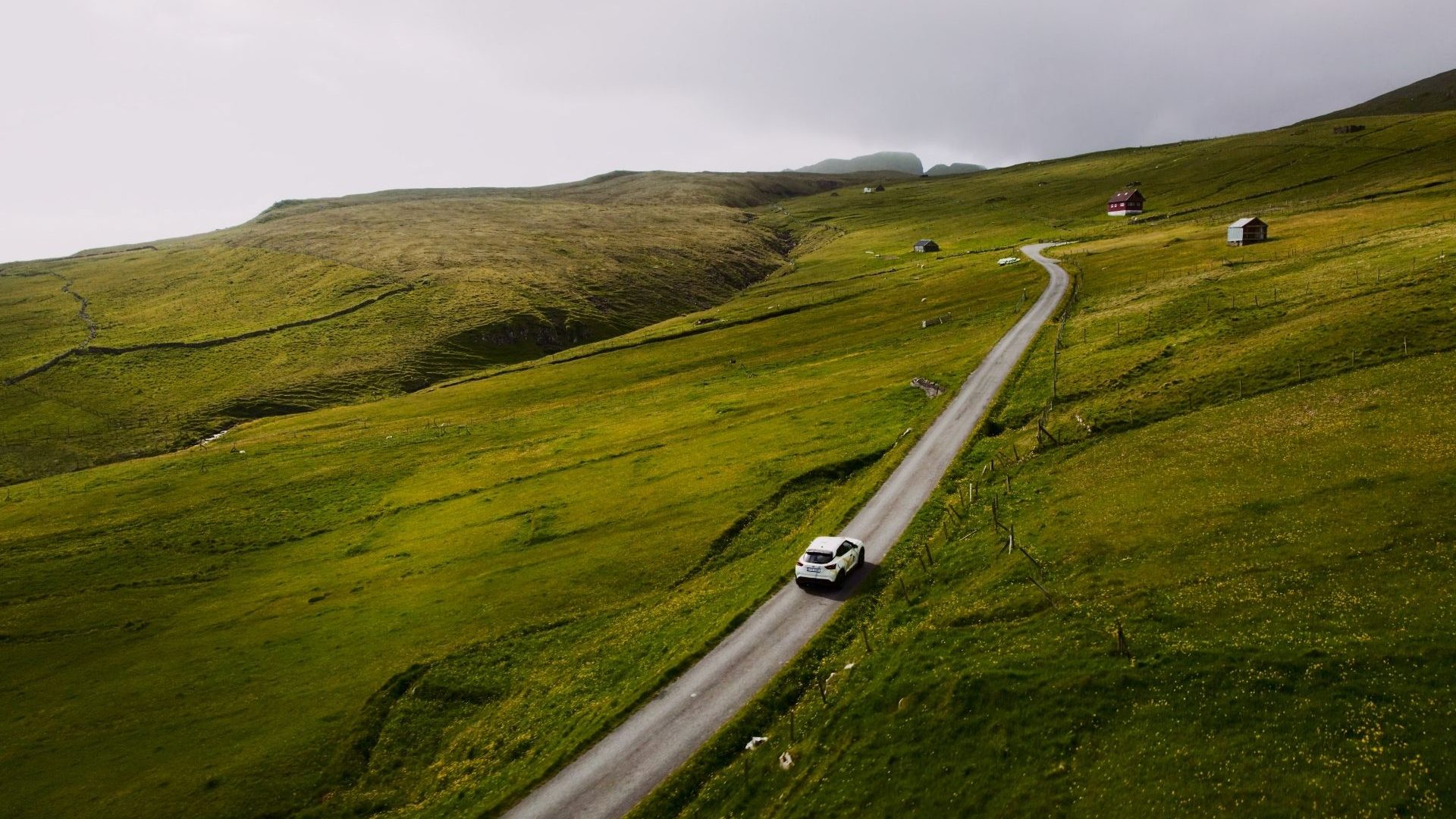 Aerial view of a car driving on a straight road through a green landscape.